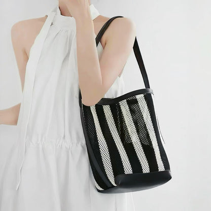 Model carrying the small black and white striped raffia bucket bag as shoulder bag.